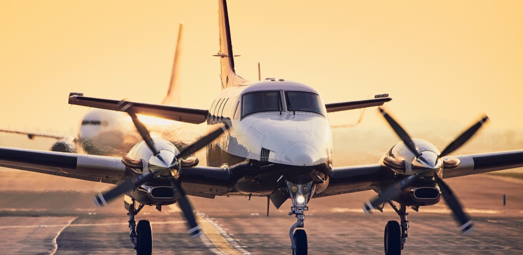 Modern propeller plane against commercial airplane on runway. Traffic at airport during sunset.